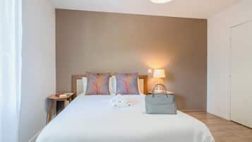 Un lit bien fait, avec des oreillers, une lampe de chevet, une petite table sur laquelle repose un livre et un sac à main.