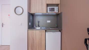 A compact kitchenette with a microwave, sink, and dishwasher, wooden cabinets, and a round mirror.