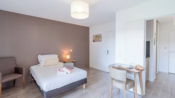 Une chambre d’hôtel moderne équipée d’un lit, d’une table de chevet, d’une chaise et d’un bureau avec une autre chaise.