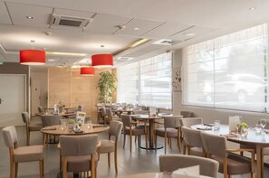 A modern dining area with round tables and chairs, red pendant lights, and large windows with blinds. - Quality Aparthotel Lyon L'isle-dabeau (L'Isle-d'Abeau)