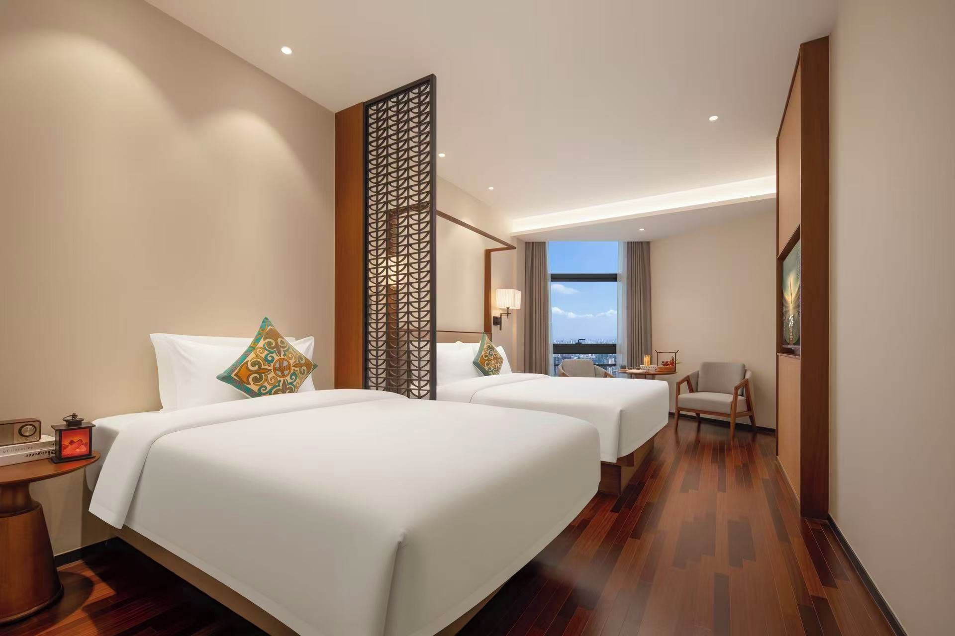 A hotel room with two beds, a nightstand, a chair, and a view of the cityscape.
