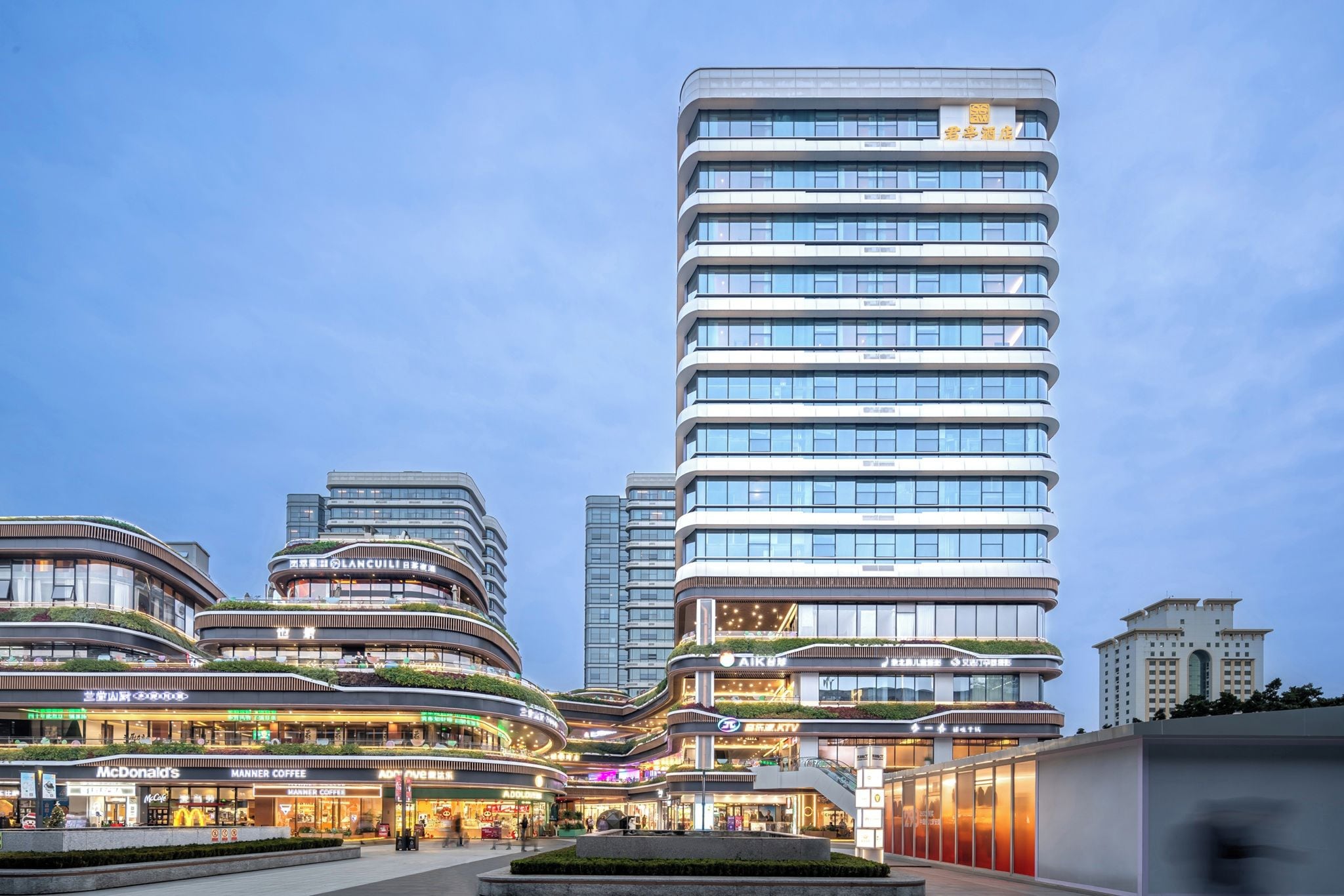 A modern multi-story building with a curved facade, featuring various commercial spaces on the ground floor.