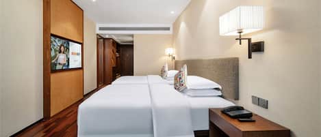 A hotel room with two beds, a wooden floor, a nightstand with a phone, and a wall-mounted lamp.