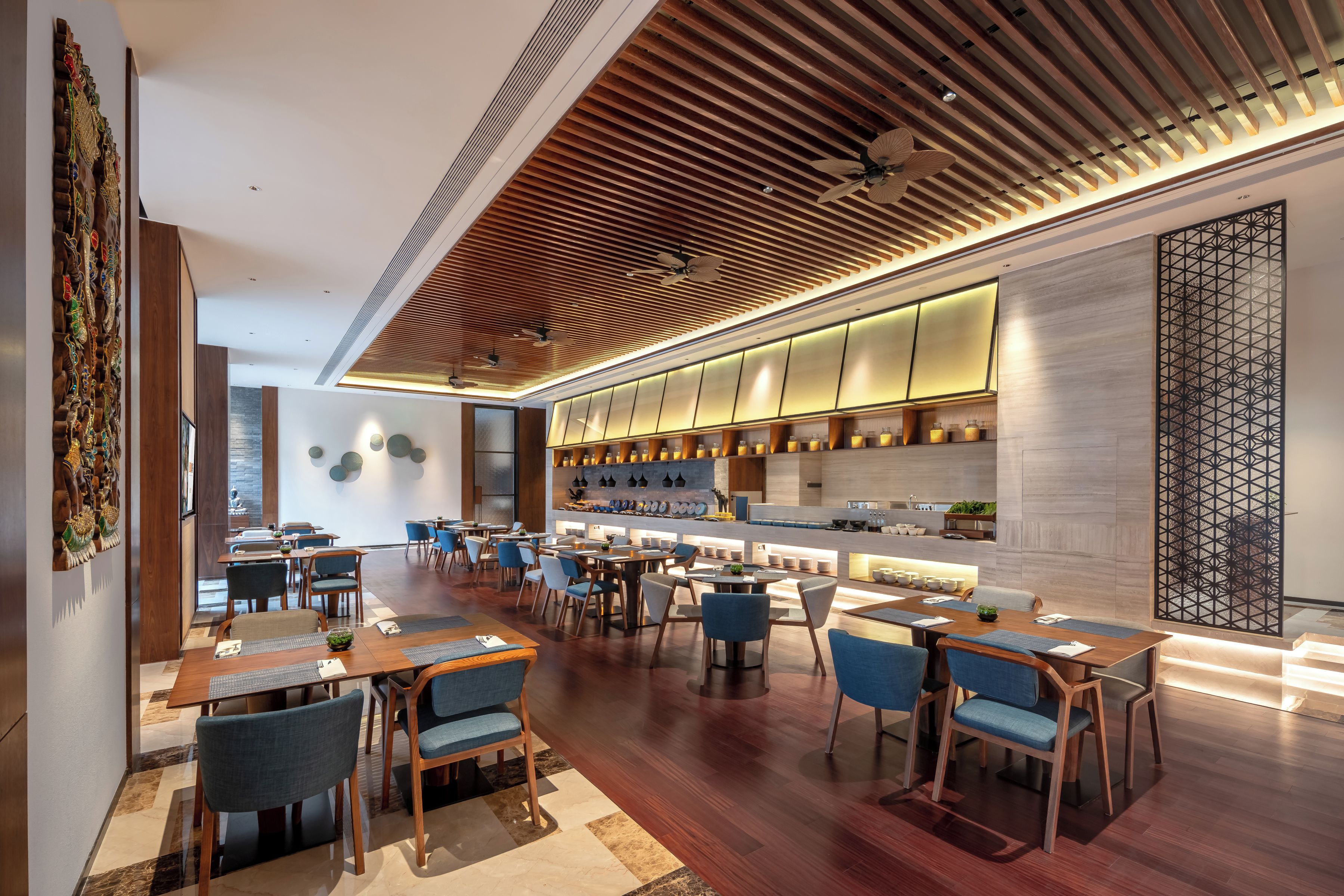 Un restaurante moderno con suelo de madera, sillas tapizadas en azul y una larga barra con cocina a la vista.