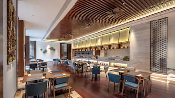 Un restaurante moderno con suelo de madera, sillas tapizadas en azul y una larga barra con cocina a la vista.