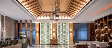 A spacious lobby with a high ceiling, a reception desk, seating area, and a patterned wall.