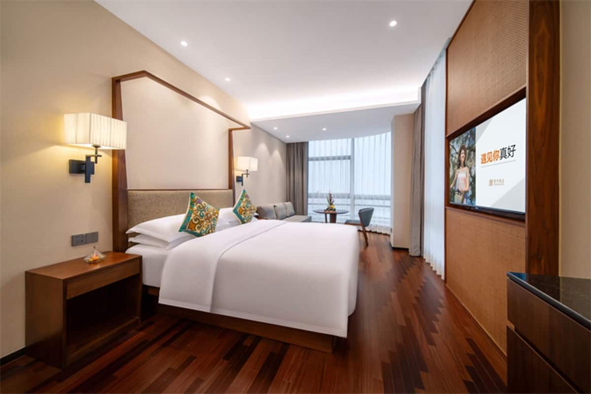 Habitación de hotel moderna con una cama grande, lámparas de noche, una mesita y vistas a la ciudad.