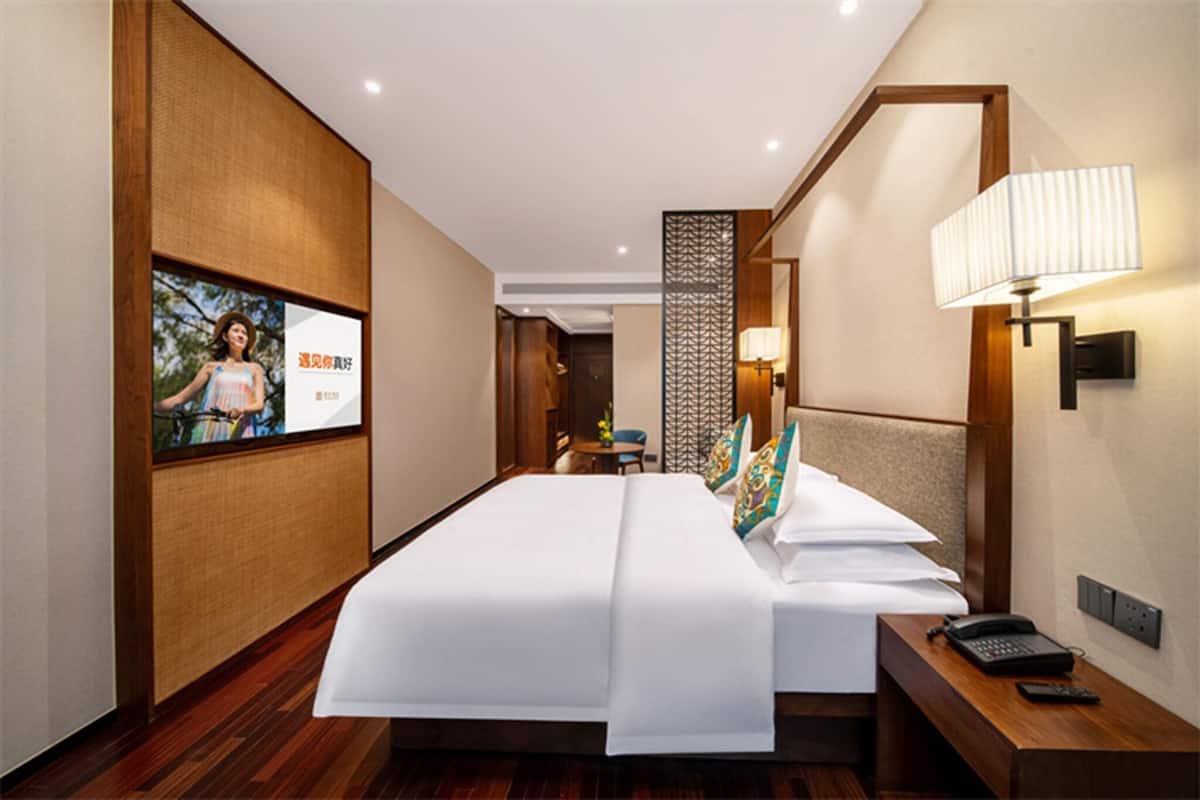Habitación de hotel con una cama grande, una mesita de noche con lámpara, teléfono y televisor montado en la pared.