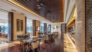 Un restaurante espacioso con piso de madera, diseño moderno de techo y una larga barra con asientos.