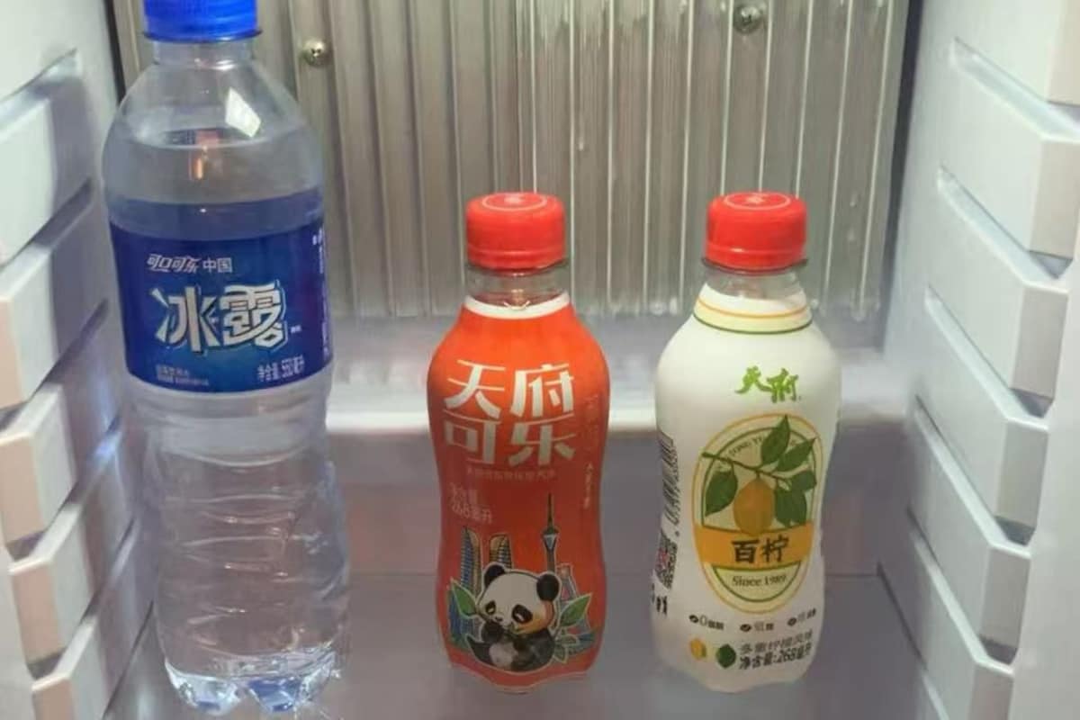 A refrigerator shelf with three bottles: a clear water bottle, a red bottle with a panda, and a white bottle with a pear.