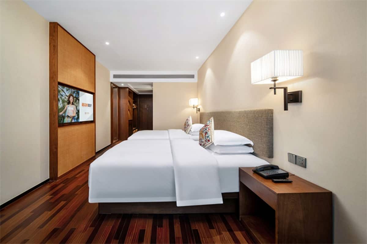 Habitación de hotel con dos camas, piso de madera, mesita de noche con teléfono y una lámpara de pared.