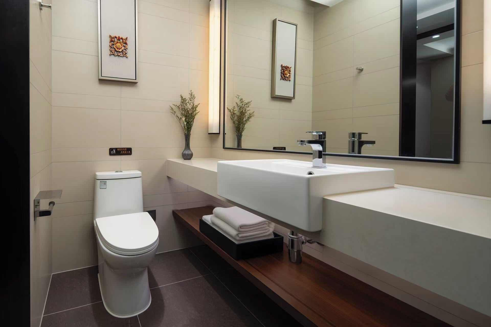 Een moderne badkamer met een wit toilet, een grote wastafel met een spiegel erboven en een klein plankje met handdoeken.
