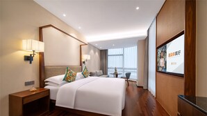 Ein modernes Hotelzimmer mit einem großen Bett, Nachttischlampen, einem kleinen Tisch und Blick auf die Stadt.