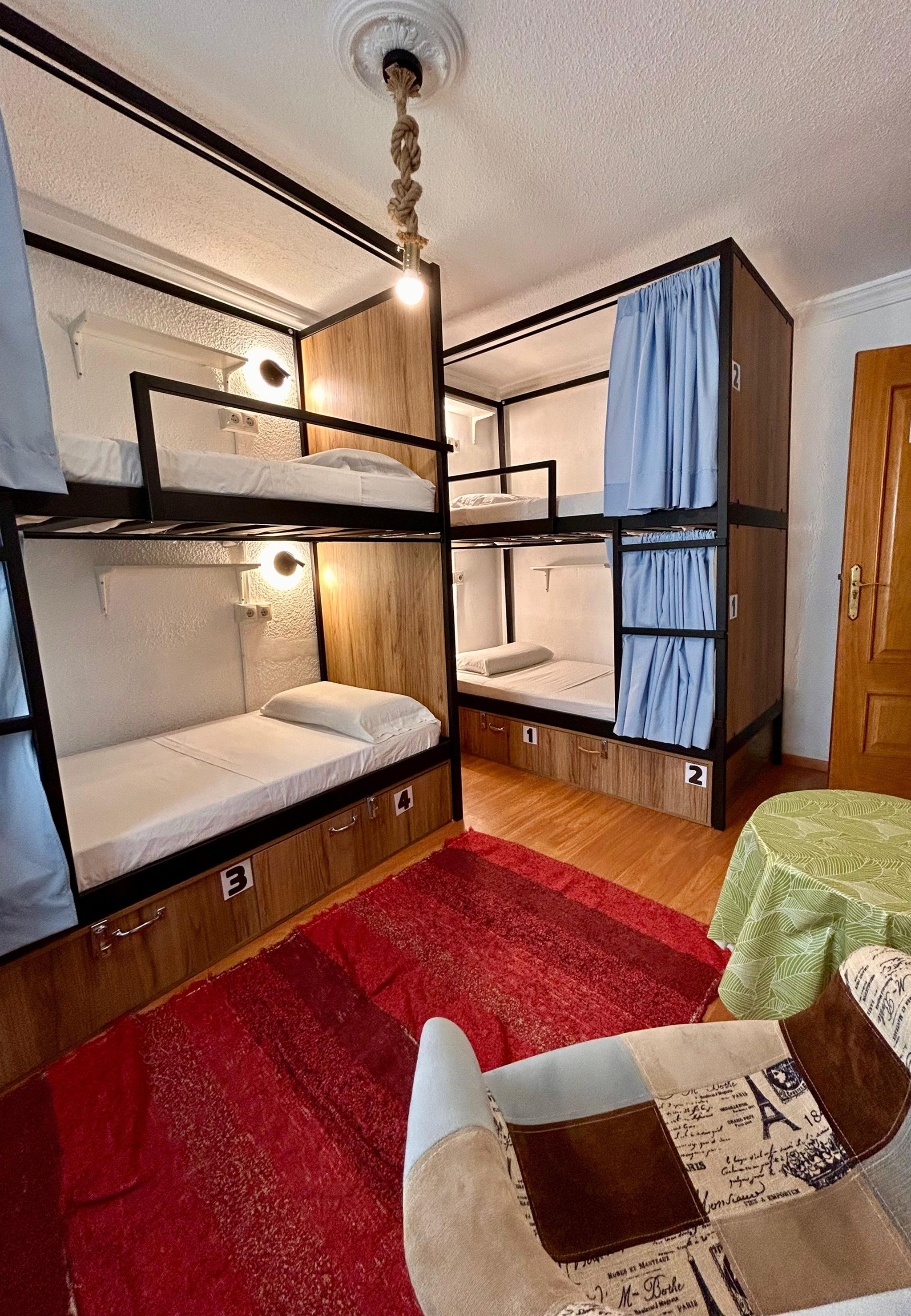 Una habitación con literas, alfombra roja y una pequeña mesa con mantel verde.