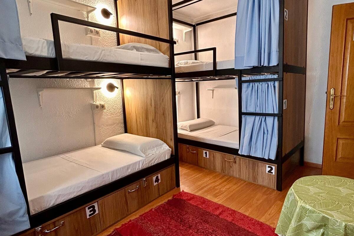 A room with bunk beds, a red carpet, and a small table with a green tablecloth.