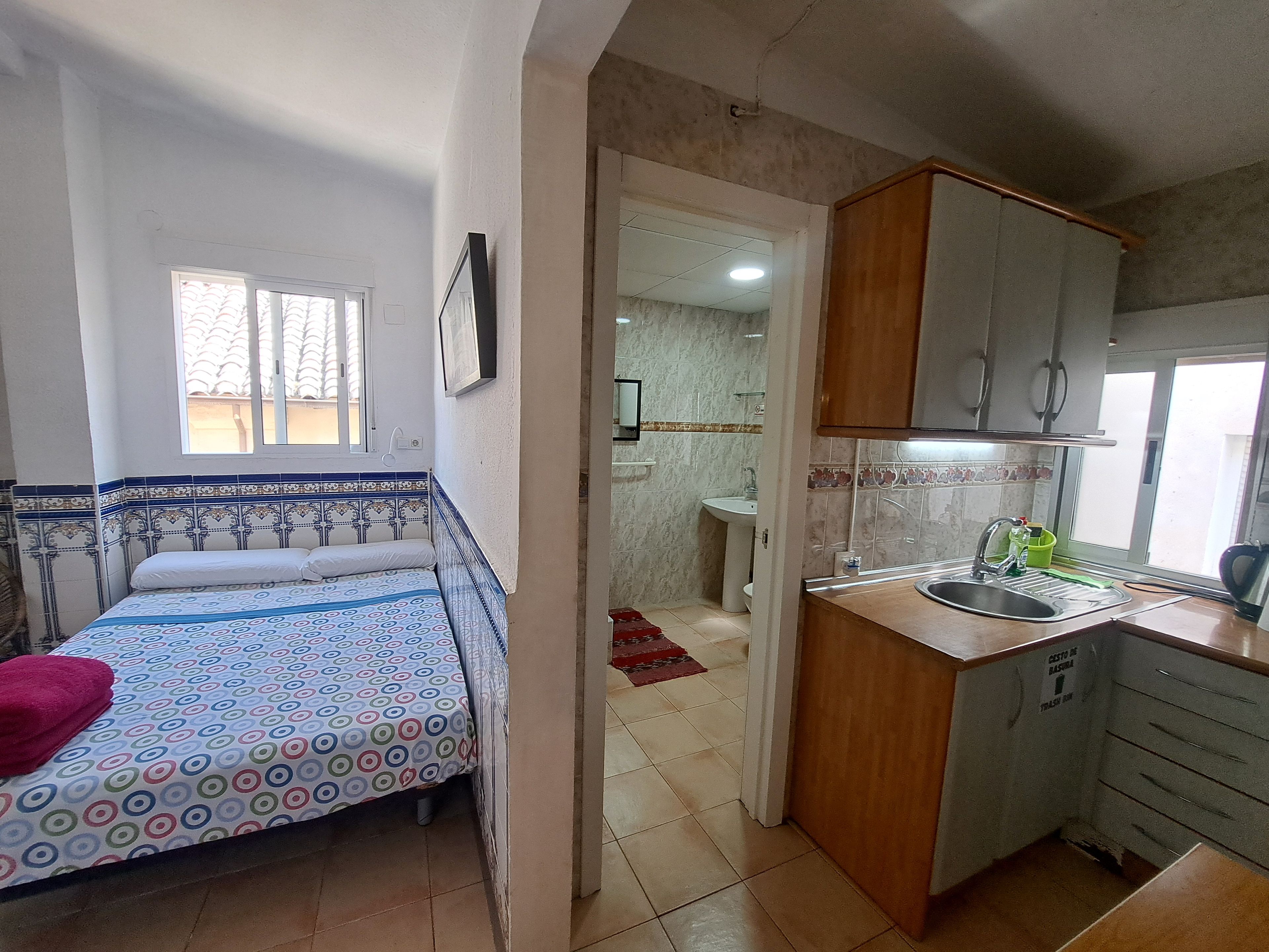 Un dormitorio con cama, ventana y baño a la vista a través de una puerta abierta.