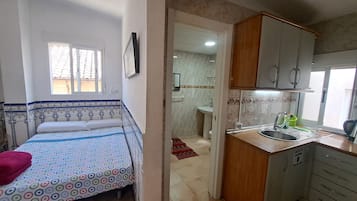 Un dormitorio con cama, ventana y baño a la vista a través de una puerta abierta.