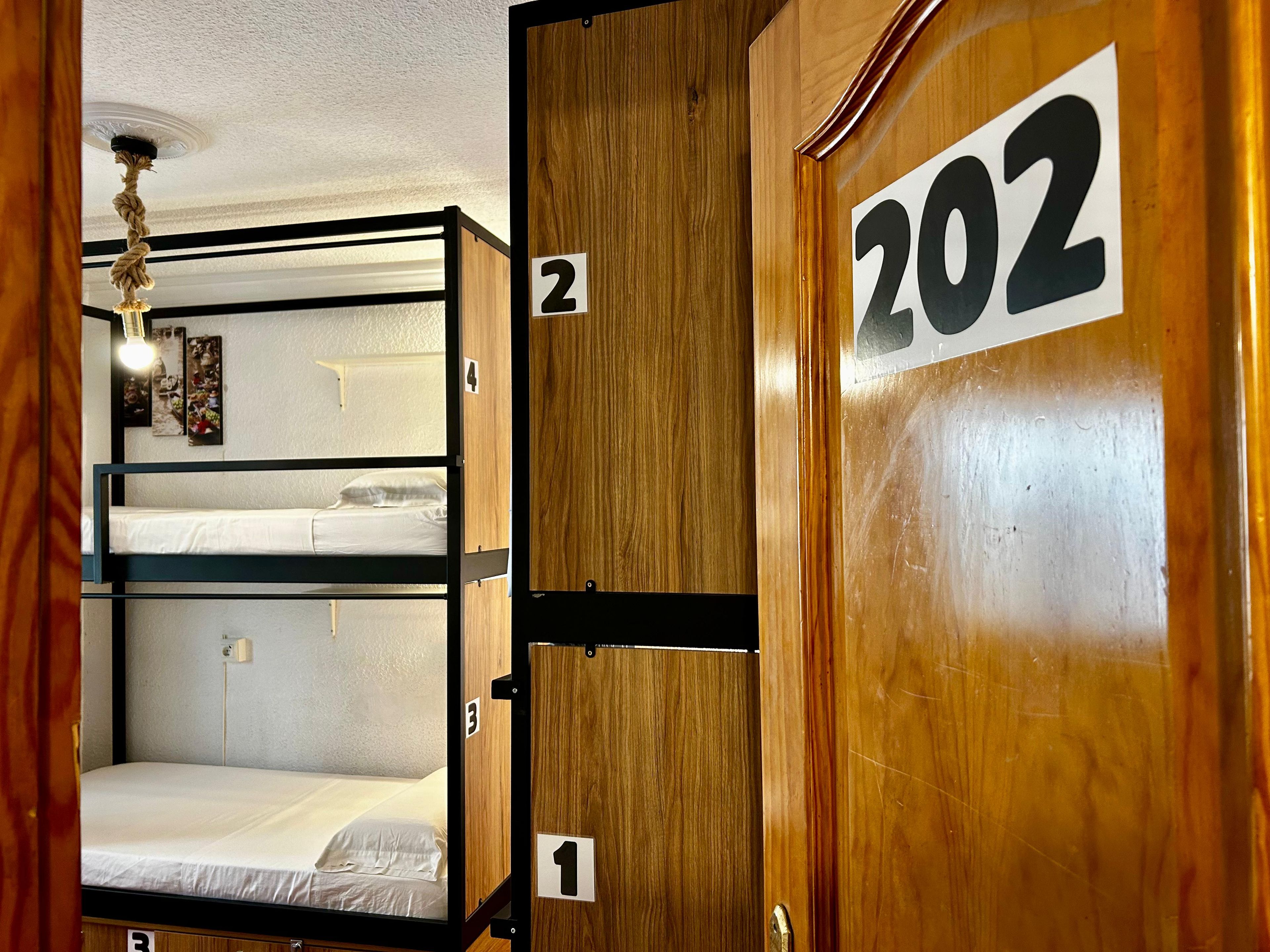 A bunk bed room with wooden walls, numbered doors, and a ceiling light.