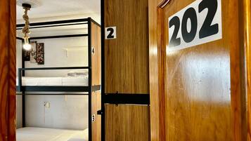 A bunk bed room with wooden walls, numbered doors, and a ceiling light.