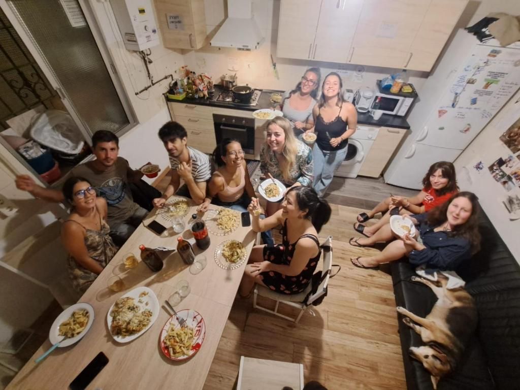 A group of people dining in a kitchen with a dining table, chairs, and a refrigerator.
