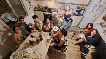 A group of people dining in a kitchen with a dining table, chairs, and a refrigerator.
