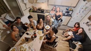 Un groupe de personnes est réuni autour d’une table dans une cuisine, avec des chaises et un réfrigérateur.