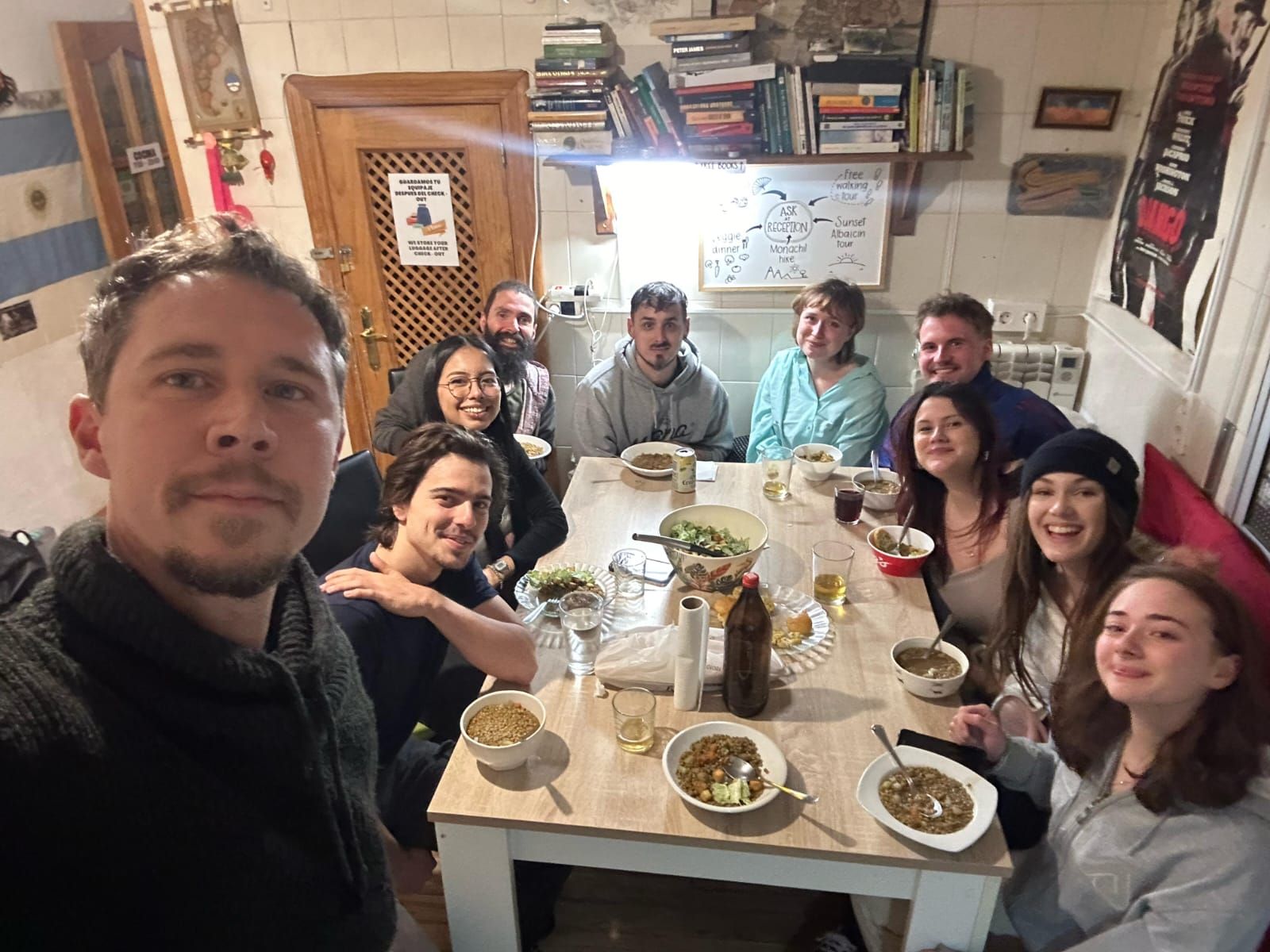 Un grupo de personas sentadas alrededor de una mesa con diferentes platos, en una habitación con una puerta de madera y una pizarra en la pared.