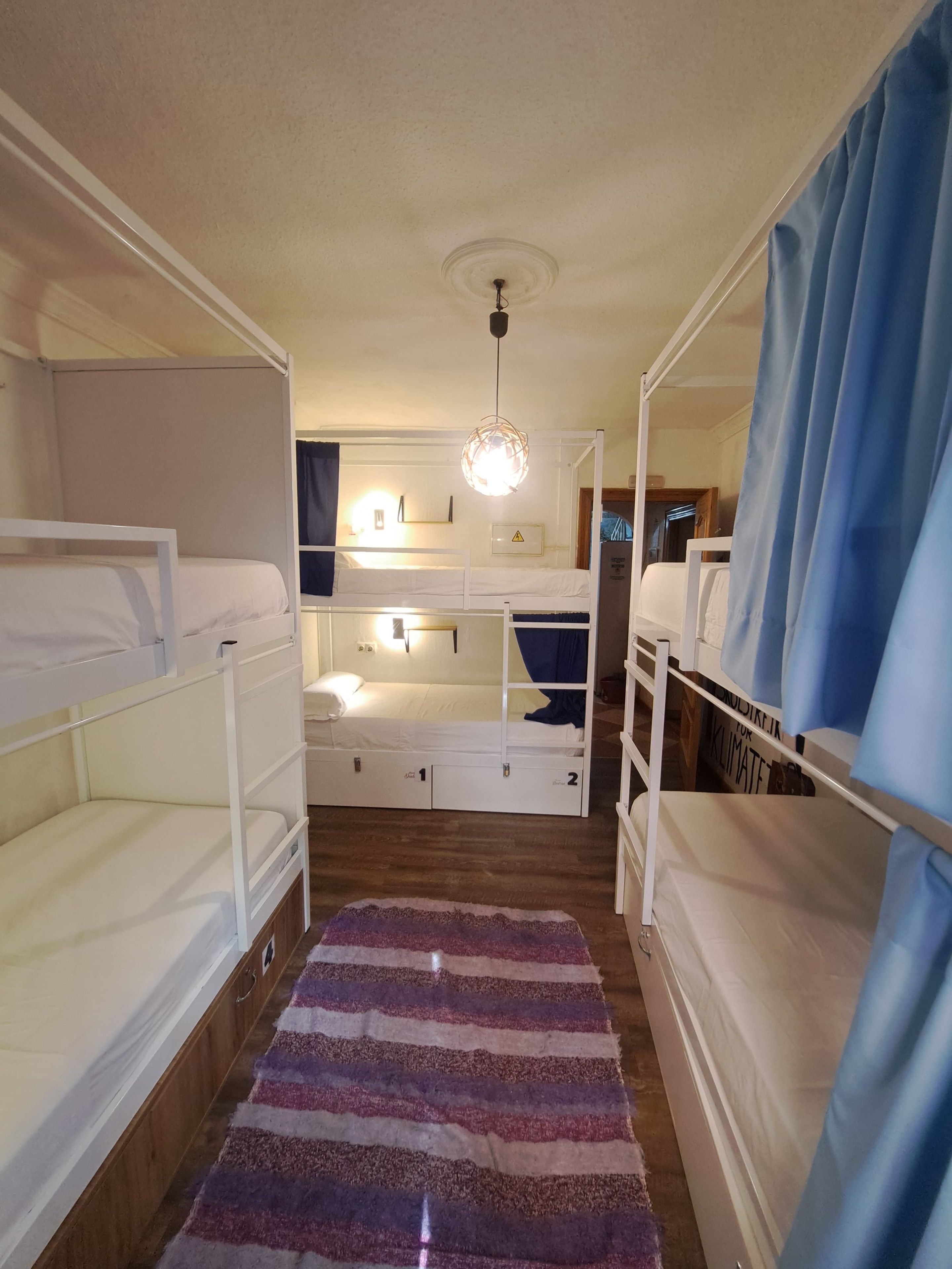 Quarto com beliche, piso de madeira, tapete listrado e luminária no teto.