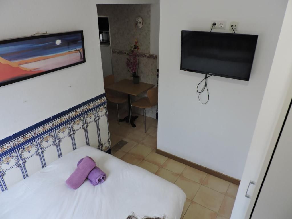 Quarto de hotel com uma cama, televisão fixada na parede, um quadro na parede e um pequeno espaço de refeições com uma mesa e cadeiras.