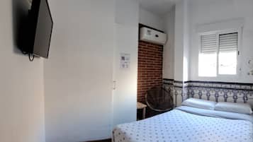 Quarto com cama, televisão na parede, janela com persianas e ar condicionado.