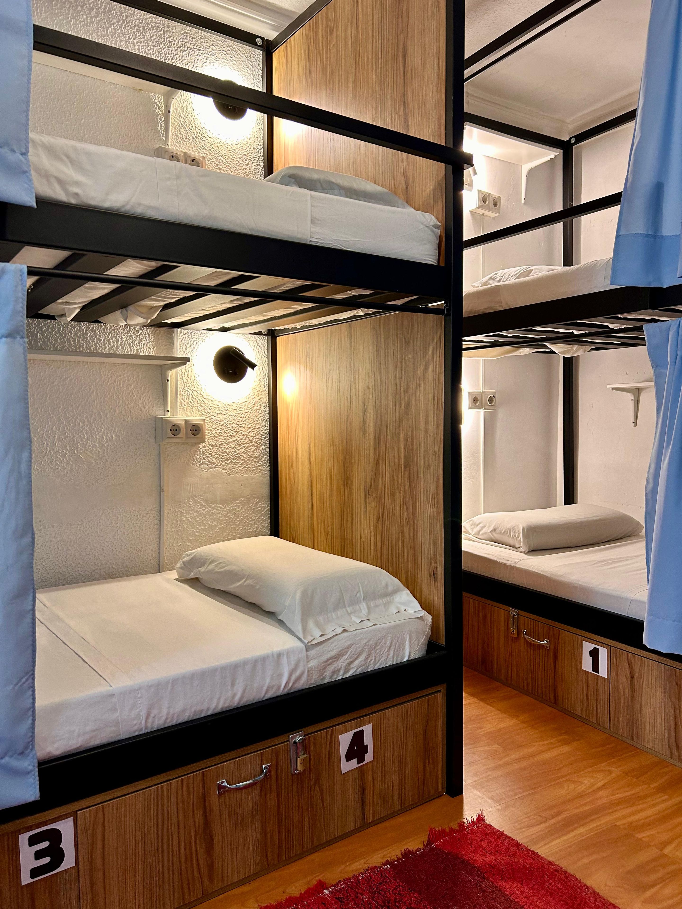 Quarto com beliches, painéis de madeira e tapete vermelho. Há compartimentos de armazenamento numerados abaixo das camas.