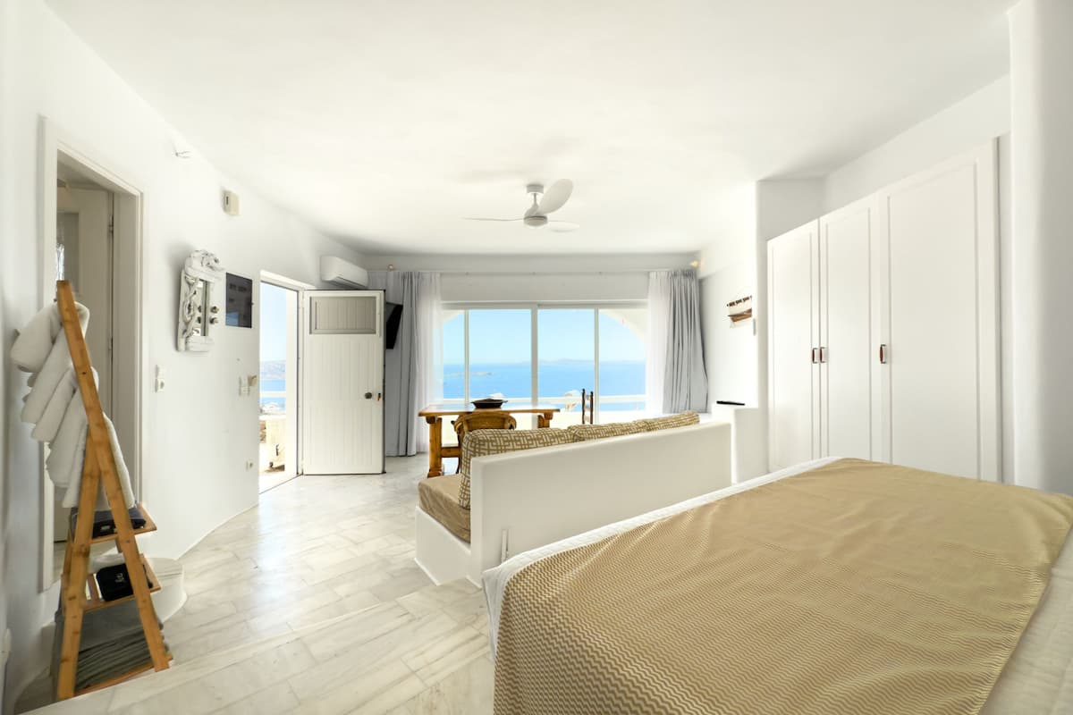 Een slaapkamer met een bed, een houten ladder, een tafel en uitzicht op zee.