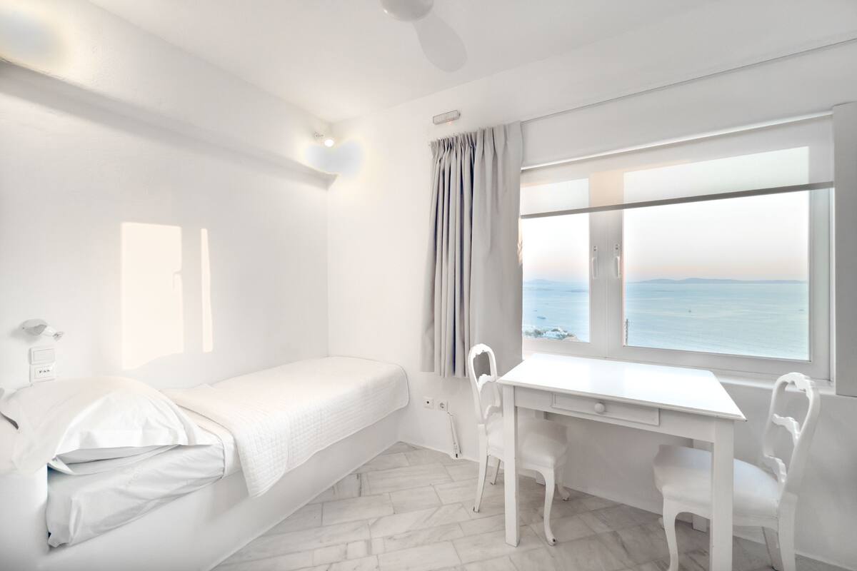 Een kamer met een bed, een bureau en uitzicht op zee.