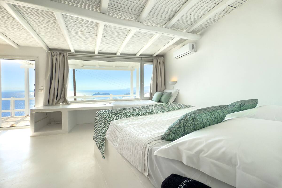 Een slaapkamer met een groot raam, een bed, een nachtkastje en een ingebouwde bank.