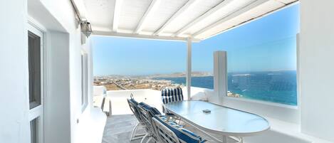 A terrace with a table and chairs, a view of the sea, and a white interior.