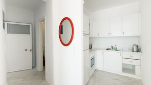 Une cuisine avec des meubles blancs, un miroir à cadre rouge et une porte blanche.