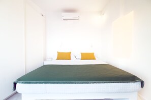 Een kleine hotelkamer met een bed, twee kussens, een groene deken en een wit hoofdeinde.
