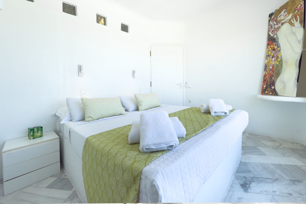 Habitació d'hotel amb llit, almoines, una tauleta de nit, un quadre i una porta.