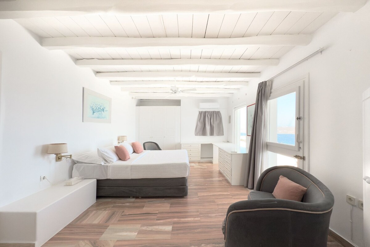 Un dormitorio con cama, mesita de noche, lámpara y vista al mar.