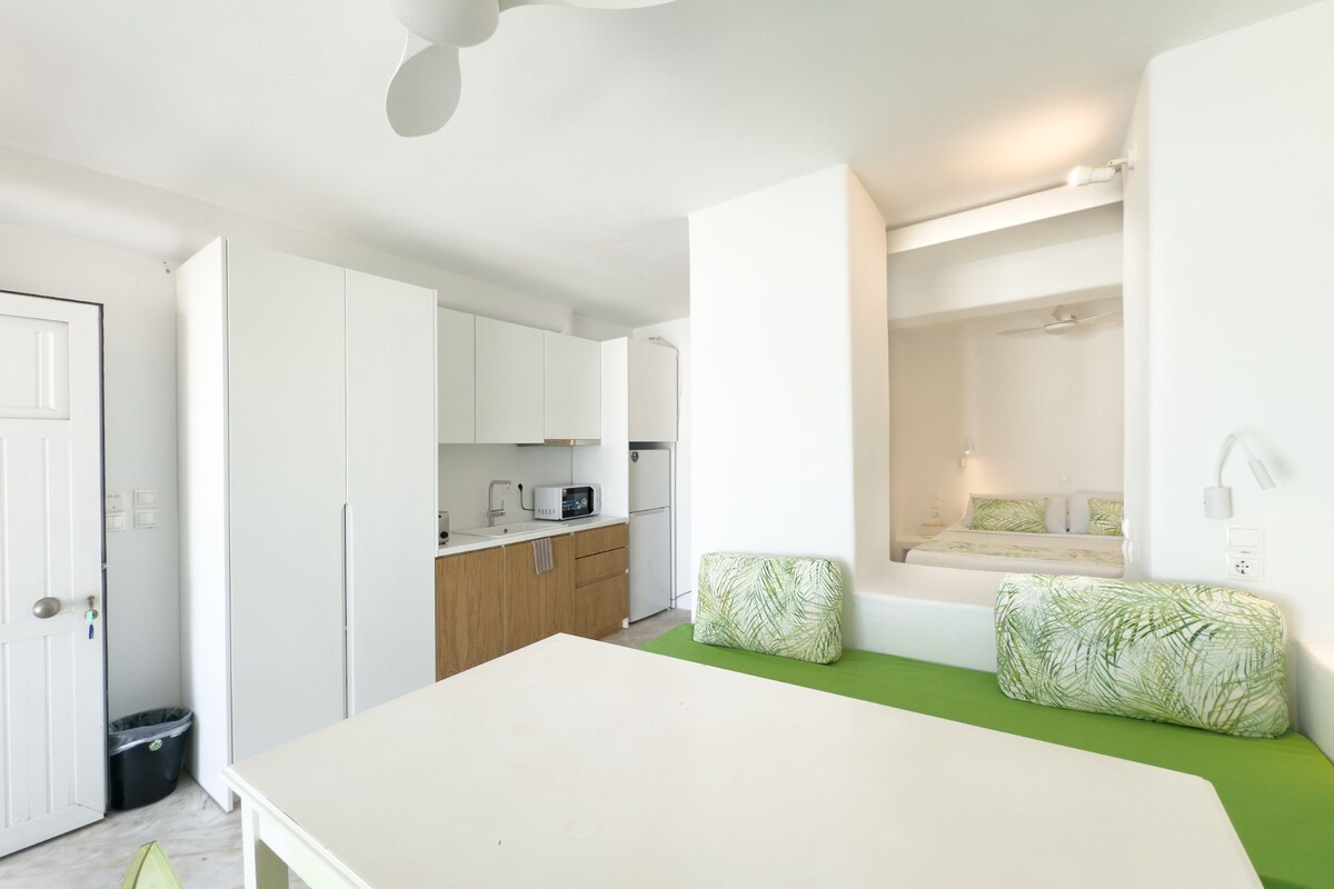 Una habitación compacta con kitchenette, una cama con ropa de cama verde y una pequeña mesa.