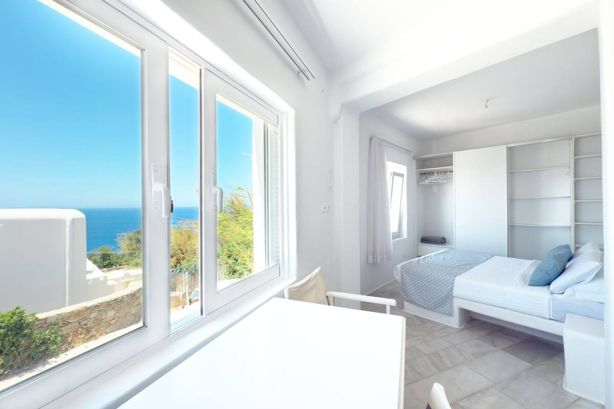 Een kamer met een bed, een tafel en uitzicht op zee.