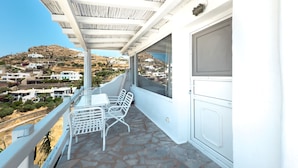 Un balcon avec une table et des chaises, une vue sur une colline parsemée de bâtiments et une porte blanche.