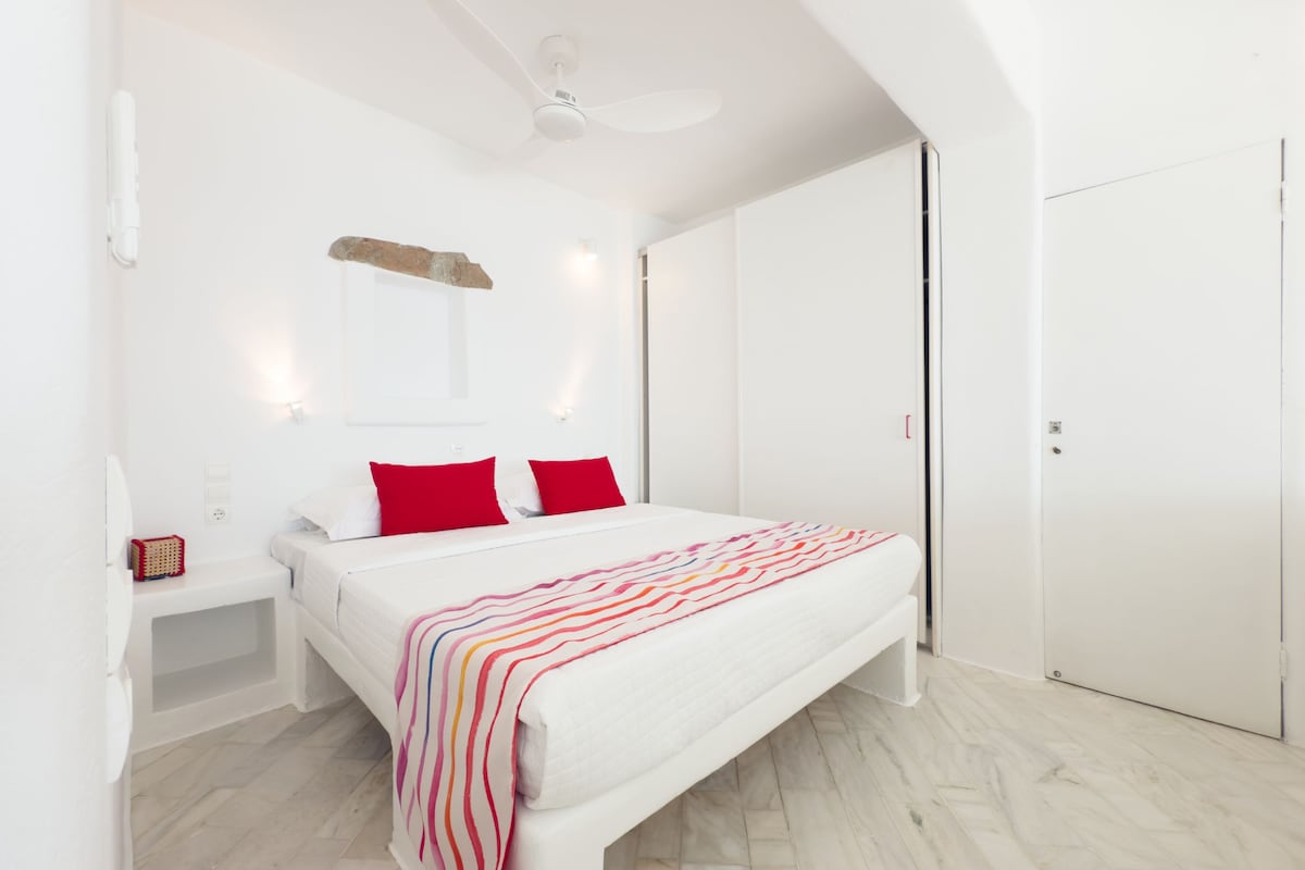 Un dormitori modern amb un llit gran, parets blanques i un ventilador de sostre.
