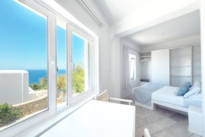 Una habitació amb un llit, una taula i vista al mar.