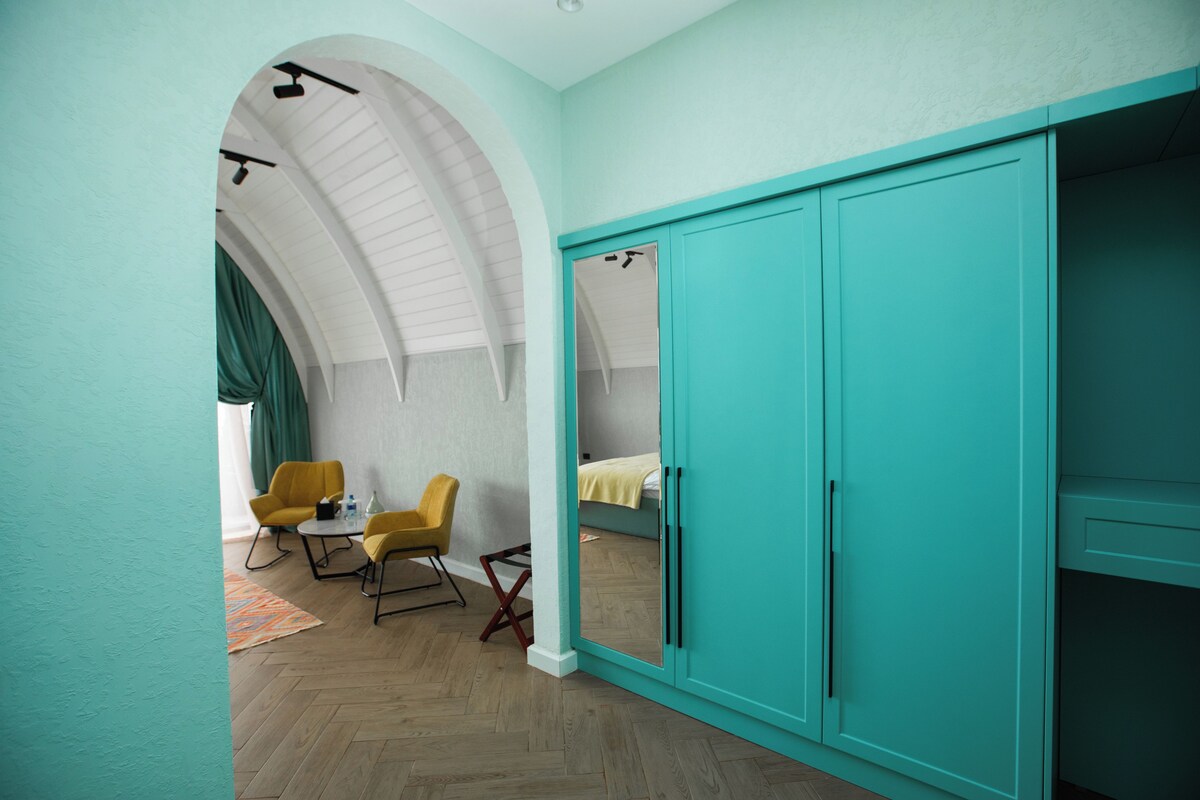 A room with teal walls, a large wardrobe, a bed, and two yellow chairs.