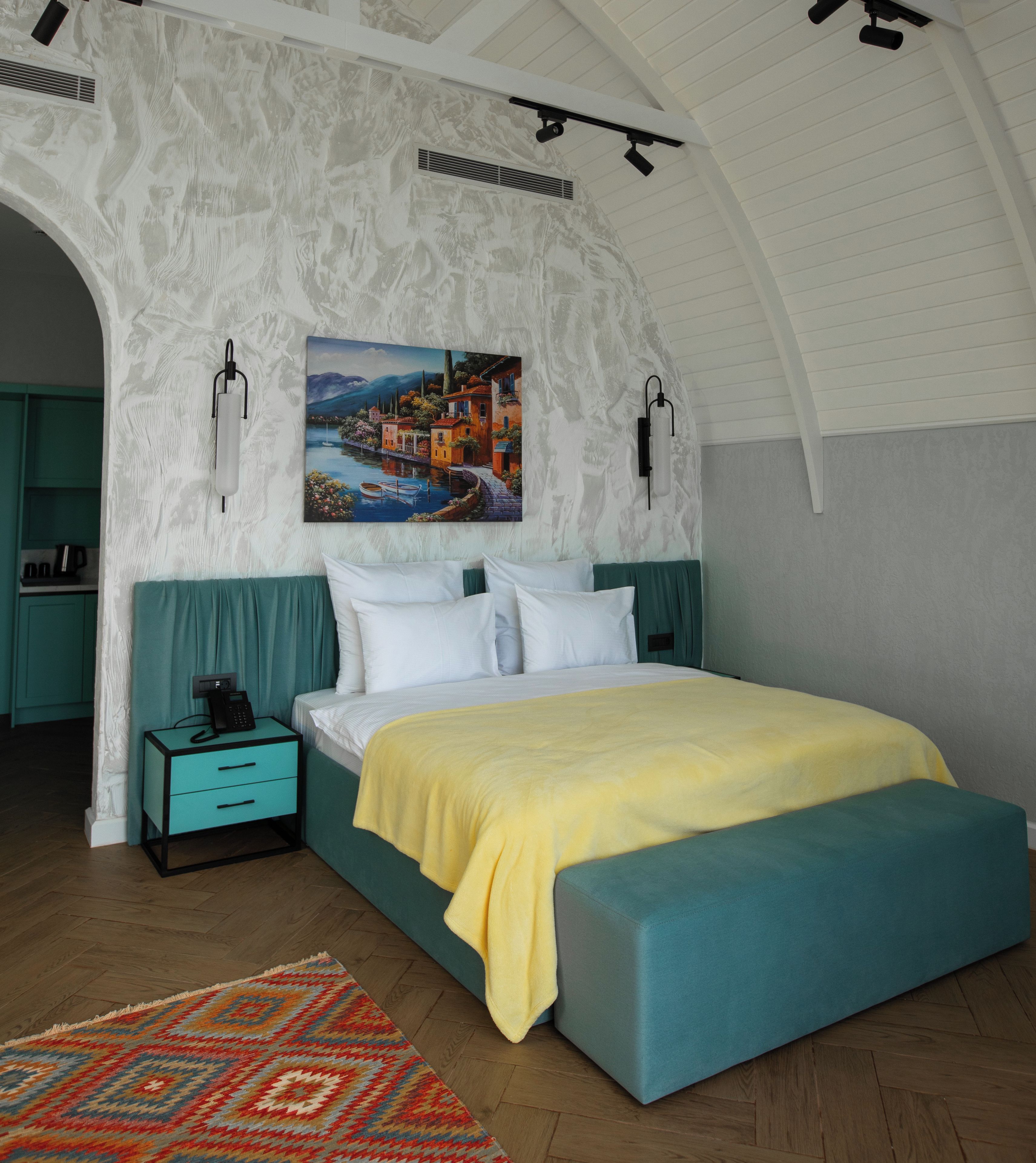 Een slaapkamer met een bed, een nachtkastje, een schilderij en uitzicht op een meer.