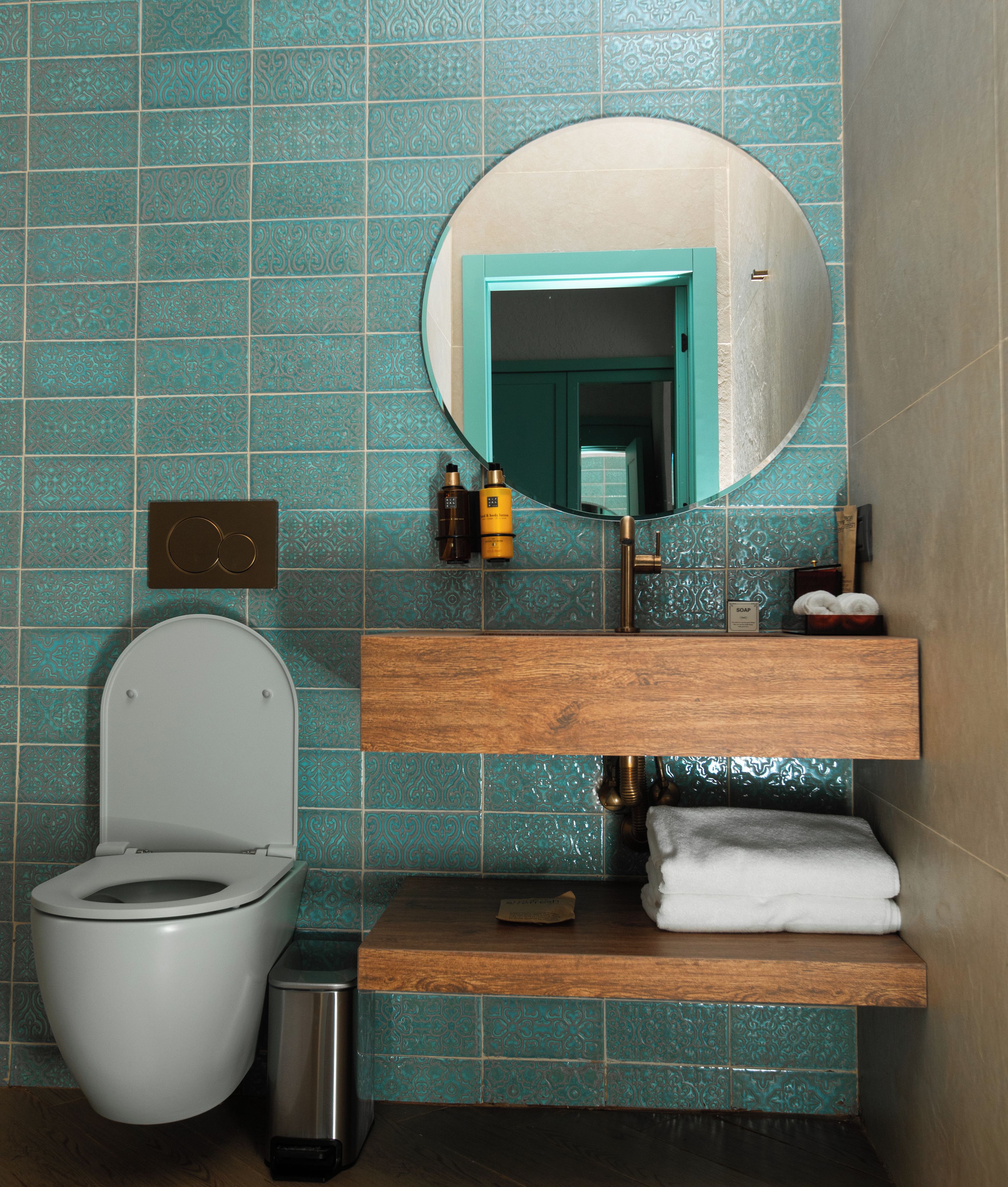 Een badkamer met toilet, wastafel, spiegel en decoratieve tegels.
