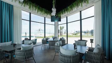 A spacious indoor area with large windows, wicker furniture, and a view of the beach and cityscape.