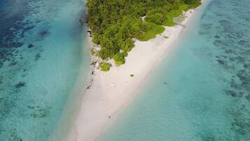 An aerial view of a beach with clear turquoise waters and a narrow strip of white sand surrounded by dense green vegetation.