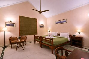 A hotel room with a bed, two chairs, a table, a ceiling fan, and wall-mounted lamps.